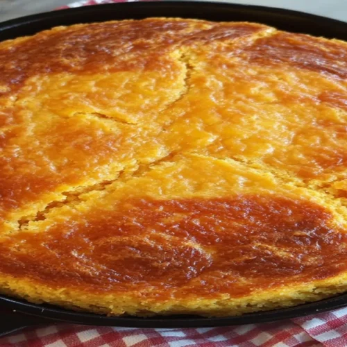 A golden-brown Southern cornbread baked in a cast iron skillet, sitting on a red and white checkered cloth.