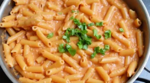 Cooked penne pasta coated in a creamy tomato and ricotta sauce, garnished with fresh parsley in a skillet.