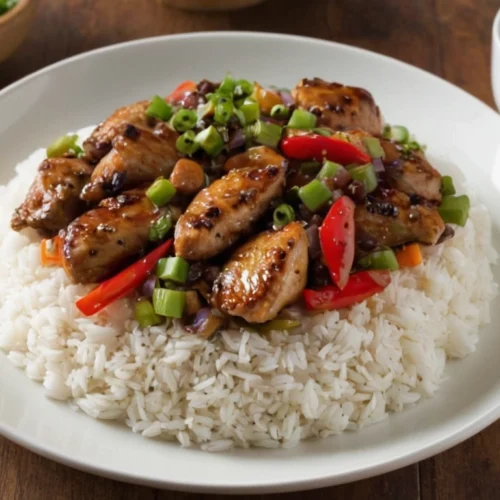 Black pepper chicken served over white rice, garnished with chopped green onions and bell peppers.