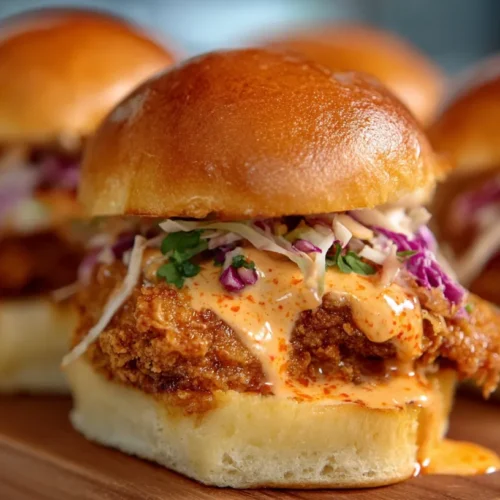 Close-up of crispy Bang Bang Chicken Sliders with creamy spicy sauce and coleslaw on soft toasted buns