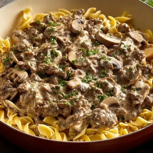 Creamy ground beef stroganoff with mushrooms served over egg noodles in a large skillet, garnished with fresh parsley.