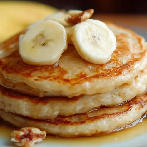 Stack of fluffy banana pancakes topped with fresh banana slices, walnuts, and maple syrup on a white plate.