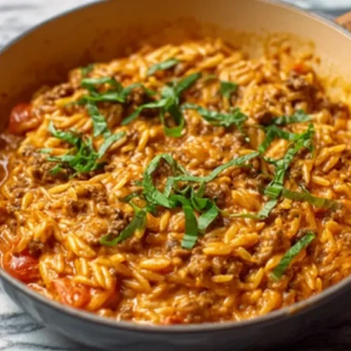 Creamy ground beef orzo with tomato cream sauce in a skillet, topped with fresh basil.
