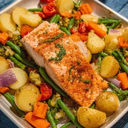 A baked sheetpan salmon fillet with roasted baby potatoes, green beans, carrots, broccoli, and cherry tomatoes, seasoned with herbs and spices.