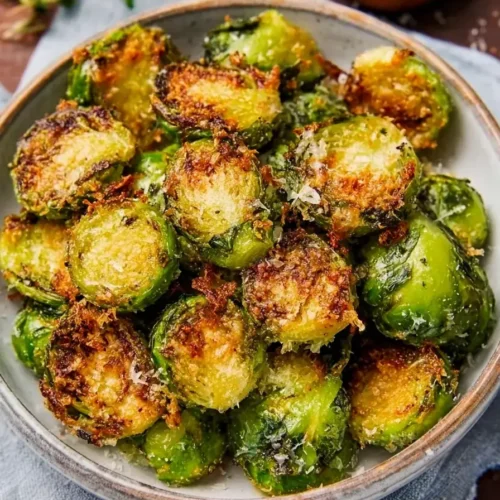 Close-up of golden brown crispy garlic parmesan Brussels sprouts served in a decorative blue bowl, topped with freshly grated cheese.