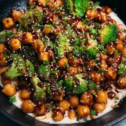 Vegan sticky sesame chickpeas with broccoli, served in a black bowl and garnished with sesame seeds and green onions.