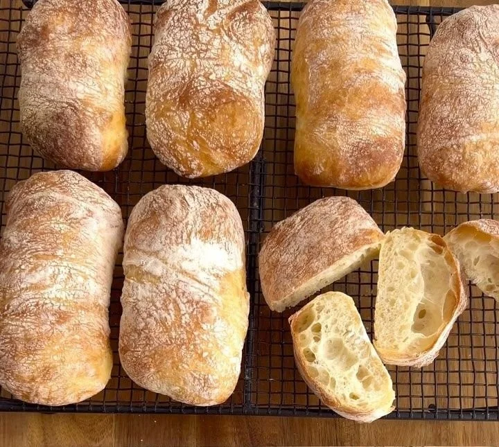 Freshly baked no-knead ciabatta with a light, airy crumb on a wooden board.
