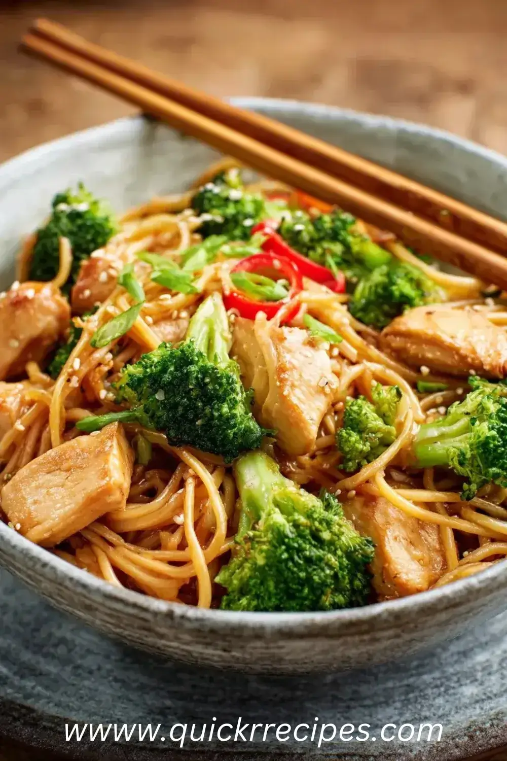 Garlic Chicken and Broccoli Noodle Bowls in blue bowl with chopsticks, broccoli, noodles and red peppers on wooden table