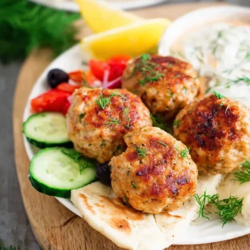 Mediterranean chicken meatballs served with tzatziki sauce, lemon wedges, fresh dill garnish, cherry tomatoes, and pita bread