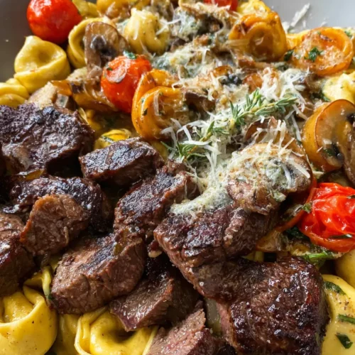 Garlic steak with creamy tortellini, mushrooms, spinach, and cherry tomatoes on white plate