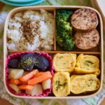 Pink bento box with mini pancakes, orange slices, apple slices with yogurt, hemp seeds, and chocolate chips.